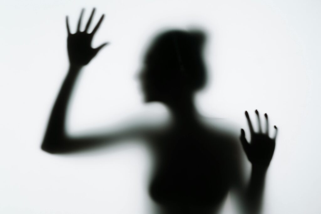 A conceptual silhouette of a woman pressing her hands against a smoky glass panel, evoking mystery.